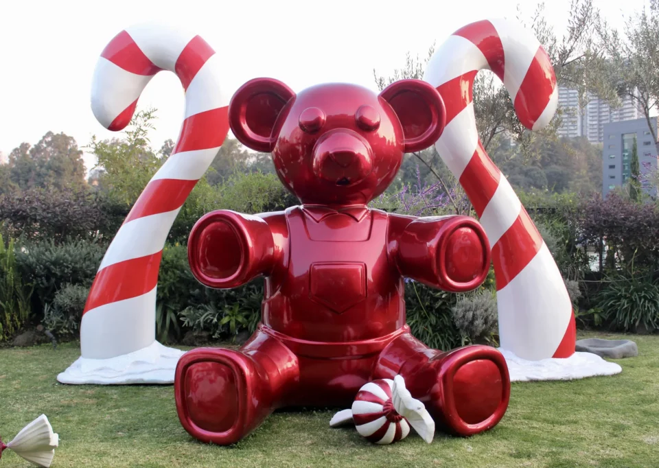 Oso rojo gigante entre bastones de caramelo en el jardín