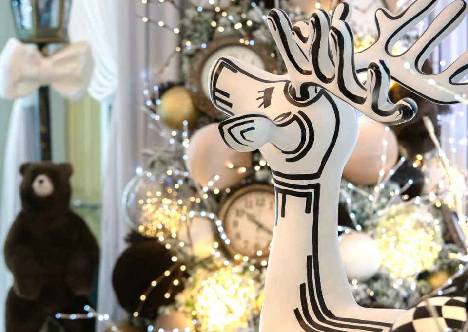 Reno blanco estilizado junto a un árbol con relojes y un oso de peluche